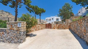 A stone-walled entrance to a property with a gated driveway leading to a white building. - Villa Despina by Villa Plus (Pefki)