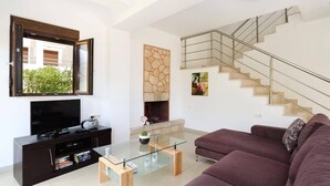 A modern living room with a flat-screen TV, a glass coffee table, a sofa, a fireplace, and a staircase. - Villa Despina by Villa Plus (Pefki)