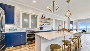 Une cuisine moderne avec des meubles bleus, un grand îlot central doté de tabourets et un éclairage suspendu.