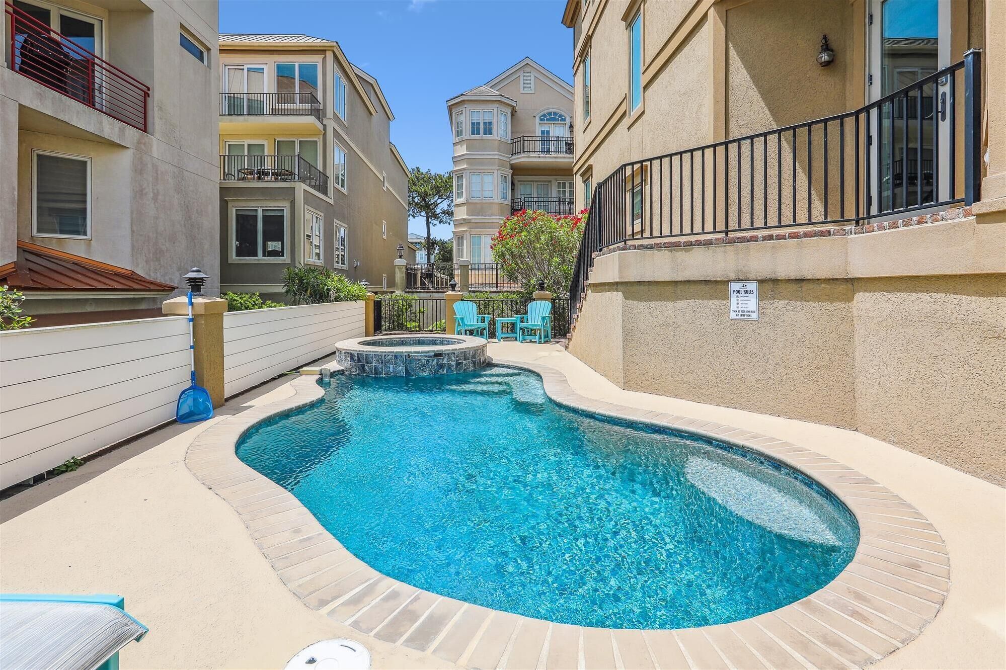 A swimming pool surrounded by apartment buildings with balconies, a small hot tub, and a sign indicating pool rules.