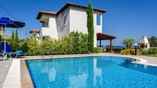 Piscina com águas azuis cristalinas, rodeada por um edifício branco com telhado vermelho e algumas espreguiçadeiras.