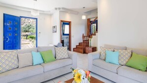 Uma sala de estar com dois sofás, uma mesa de centro com flores, uma porta azul e uma escadaria.