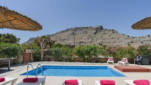A pool area with lounge chairs and umbrellas, surrounded by greenery and a mountainous backdrop. - Villa Maya by Villa Plus (Pefki)