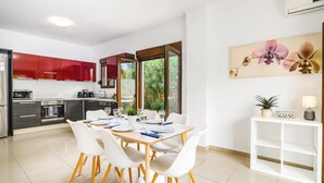 A modern kitchen with red cabinets, a dining area with white chairs, and a large window. - Villa Maya by Villa Plus (Pefki)