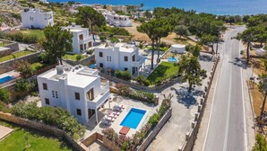 A coastal residential area with modern white buildings, a swimming pool, and a clear view of the sea. - Villa Maya by Villa Plus (Pefki)