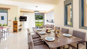 Un comedor con una mesa larga dispuesta para seis personas, un televisor montado en la pared y vistas al exterior con vegetación.