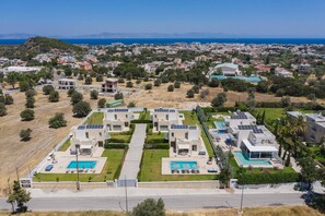 A residential area with modern houses, a swimming pool, and a view of the sea.