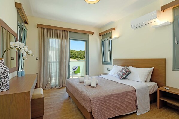 Habitación de hotel con cama, mesitas de noche, escritorio, silla, ventana con cortinas y unidad de aire acondicionado.