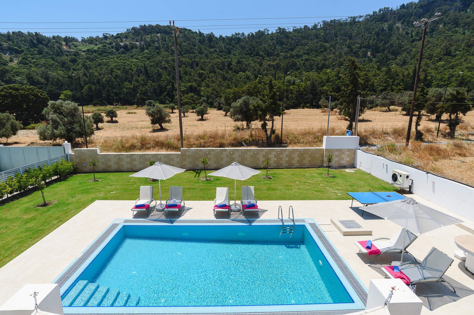 A swimming pool with lounge chairs and umbrellas, surrounded by a landscaped garden and a view of a forested hillside.