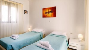 Une chambre d’hôtel avec deux lits simples, un tableau au mur, un appareil de climatisation et une fenêtre avec des rideaux.