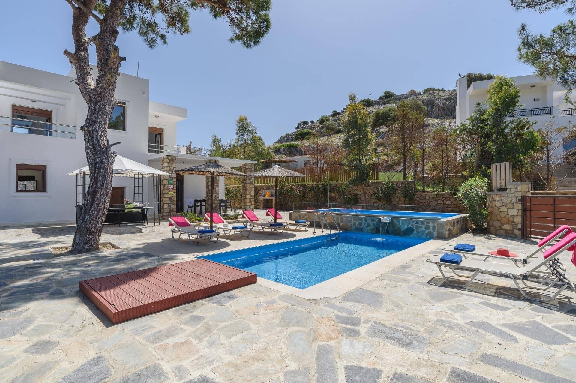 Una piscina con sillas de descanso, una terraza de madera y un patio de piedra.