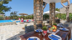 Un espace extérieur aménagé pour les repas, avec des piliers en pierre, une piscine et des chaises longues.