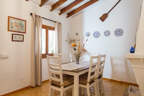 Zona pranzo con tavolo in legno e sedie bianche, una finestra con tende e piatti decorativi appesi al muro.