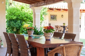 Patio esterno con tavolo di legno, sedie in vimini e piante in vaso.