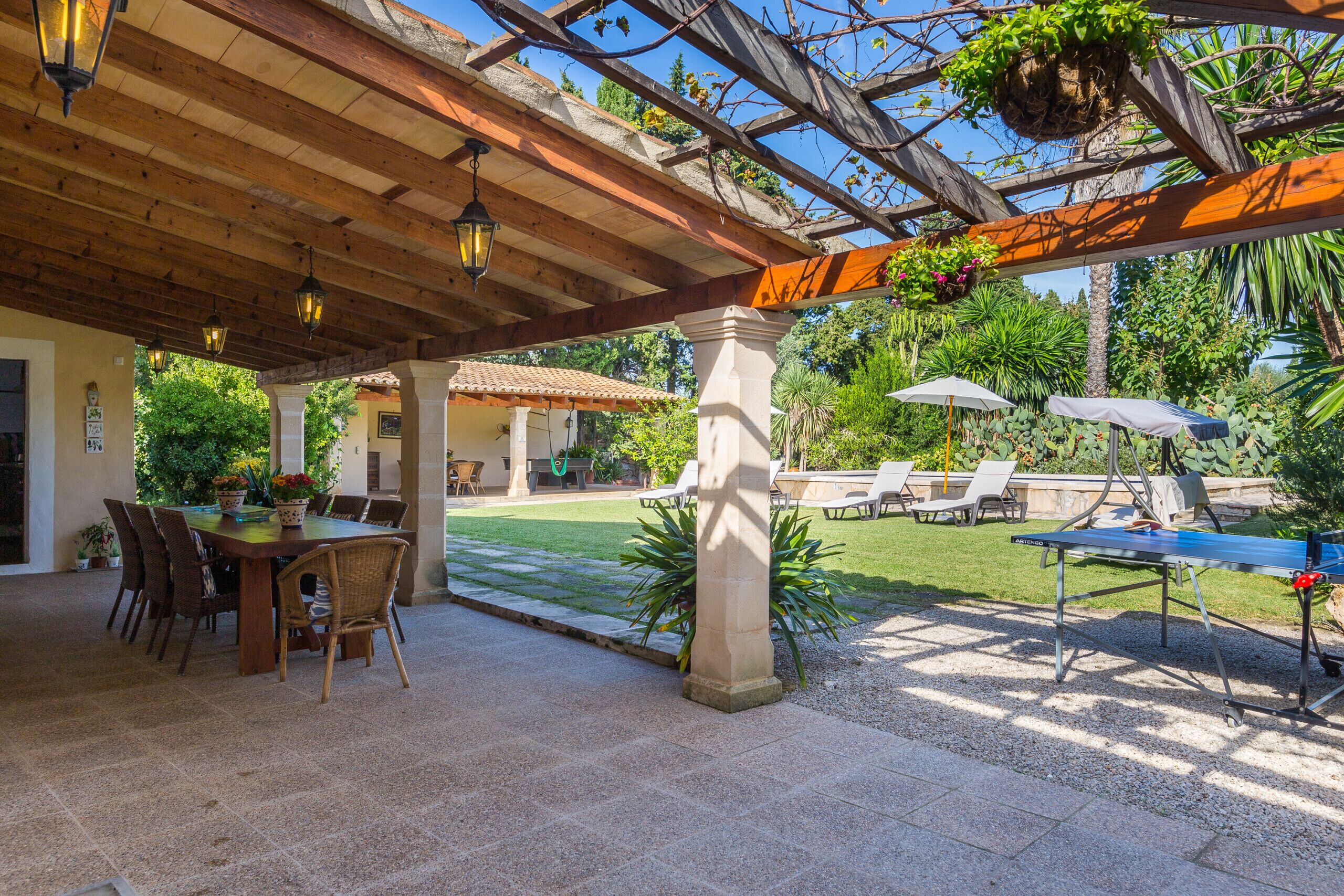 An outdoor patio with a wooden pergola, a dining table with chairs, and a pool table.