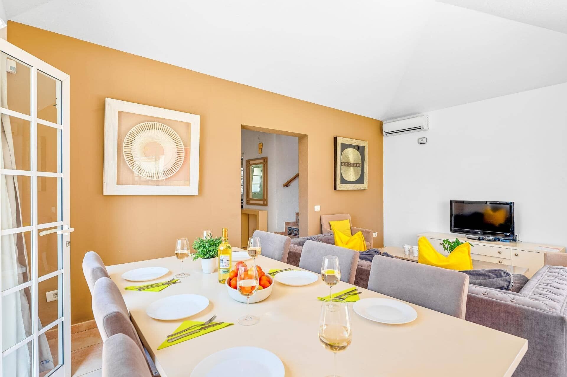 A dining area with a table set for four, a television, and a staircase leading to another room.