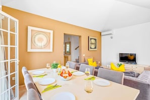 Een eetgedeelte met een tafel voor vier personen, een televisie en een trap naar een andere kamer.