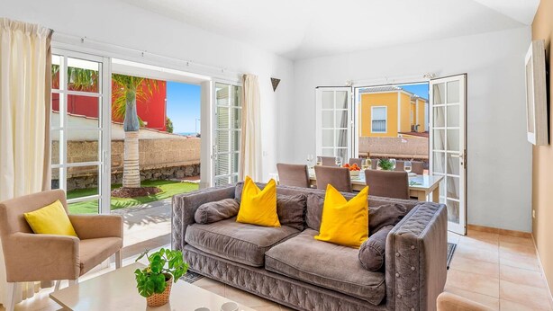 A living room with a grey sofa, yellow cushions, a coffee table, and a potted plant. - Villa Atenas by Villa Plus (Adeje)