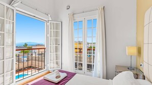 A hotel room with a bed, a window with curtains, a view of the sea, and a balcony with a pool. - Villa Atenas by Villa Plus (Adeje)
