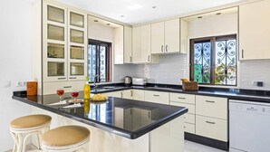 A modern kitchen with a central island, white cabinetry, and a view of greenery outside.