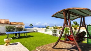 A patio with a swing, a ping pong table, and a tennis table.