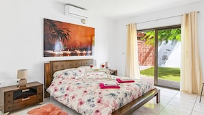 A bedroom with a bed, bedside tables, a painting, and a view of the outdoors.