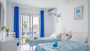 Une chambre d’hôtel avec deux lits, un bureau, une chaise, une table ornée d’un vase de fleurs et une vue sur l’extérieur.