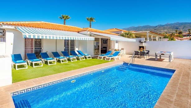 Un espace aménagé au bord de la piscine, avec des chaises longues, un barbecue et une vue sur les montagnes.