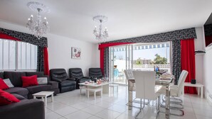 Un salon comprenant un canapé, des fauteuils, une table à manger et un balcon agrémenté de rideaux rouges.