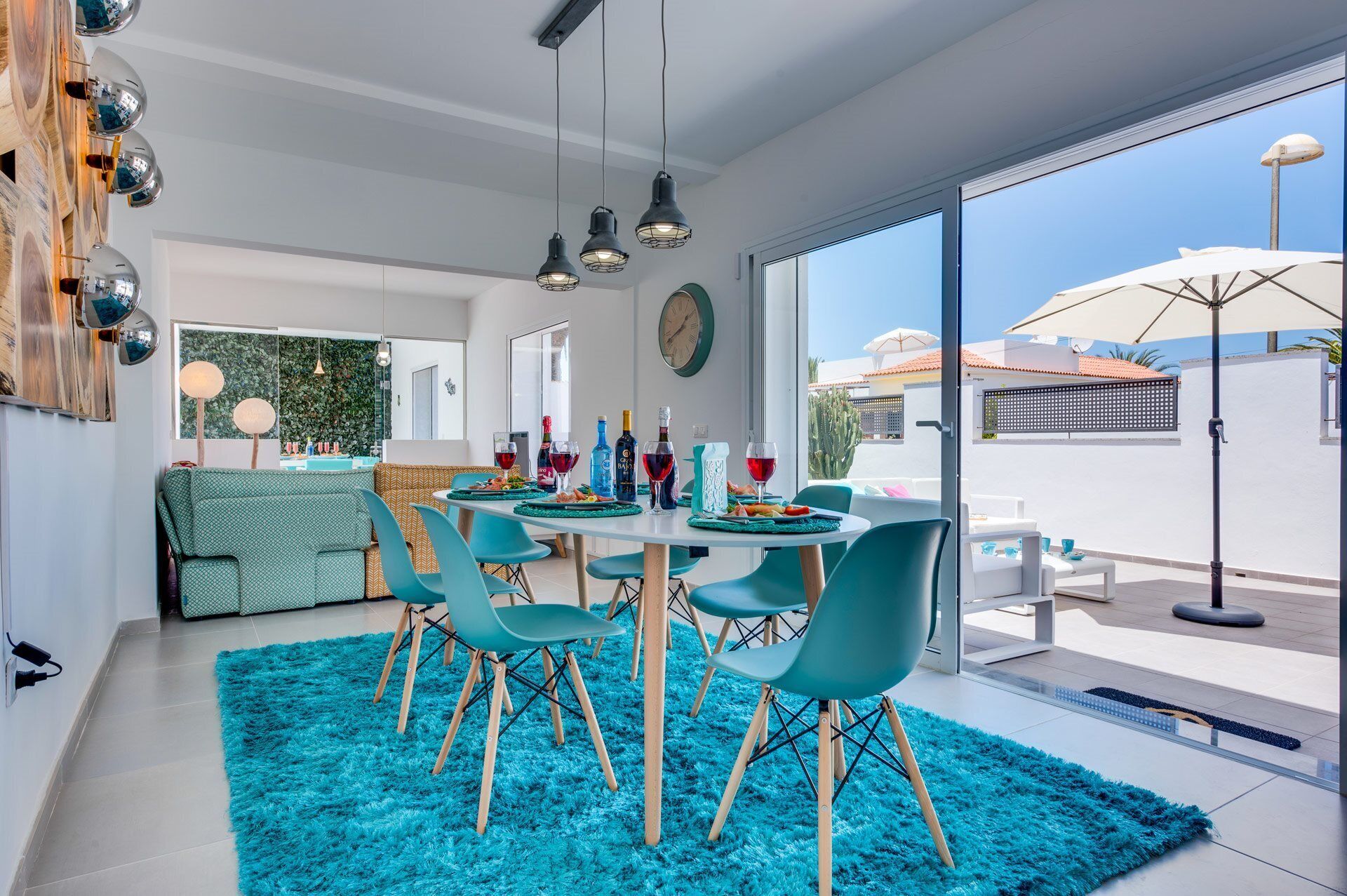 A modern dining area with a round table, teal chairs, and a blue shag rug.