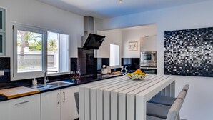 A modern kitchen with white cabinetry, a central island, and a dining area with a chair. - Villa Colibri by Villa Plus (Palm-Mar)