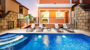 A swimming pool with lounge chairs and a building with a balcony. - Villa Isotta by Villa Plus (Adeje)
