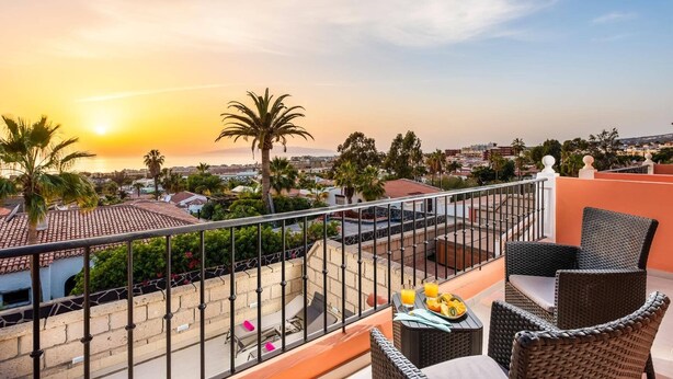 A balcony with wicker furniture, a view of the city, and palm trees. - Villa Isotta by Villa Plus (Adeje)