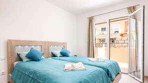 A bedroom with a wooden headboard, two beds with blue bedding, a pair of white towels, and a sliding glass door leading to an outdoor balcony. - Villa Isotta by Villa Plus (Adeje)