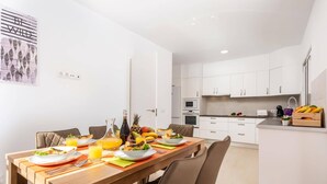 A modern kitchen with white cabinets, a dining area with a wooden table, and a kitchen island with fruits and a coffee machine. - Villa Isotta by Villa Plus (Adeje)