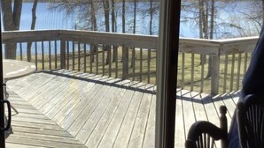 Une terrasse en bois dotée d’une rambarde, qui offre une vue sur une étendue d’eau et des arbres.