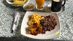 A plate with scrambled eggs, black beans, fried plantains, and sliced avocado on a table with a patterned tablecloth. - Escapada a Tortuguero  (Guapiles)