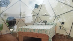 A tent-style room with a bed, a small table with a plant, and a bench. - Escapada a Tortuguero  (Guapiles)