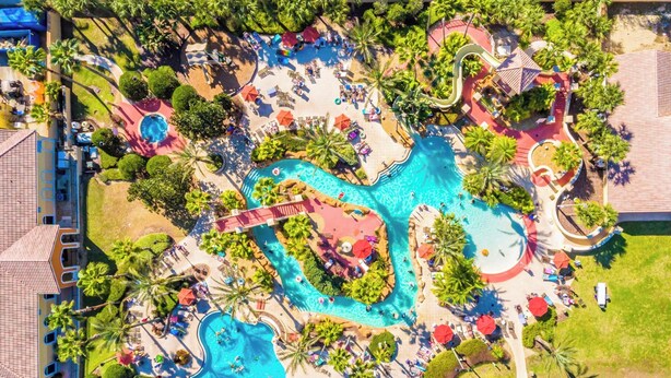 Vista aérea de un resort con varias piscinas, palmeras y tumbonas.