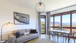 Un salon moderne comprenant un canapé, une table à manger avec des chaises, une grande fenêtre offrant une belle vue et un luminaire suspendu.