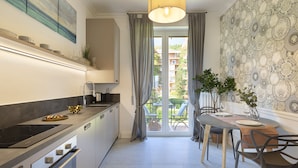 Une cuisine moderne dotée d’une cuisinière intégrée, un coin repas avec une table et des chaises, et une vue sur un balcon agrémenté d’une table et de chaises vertes.