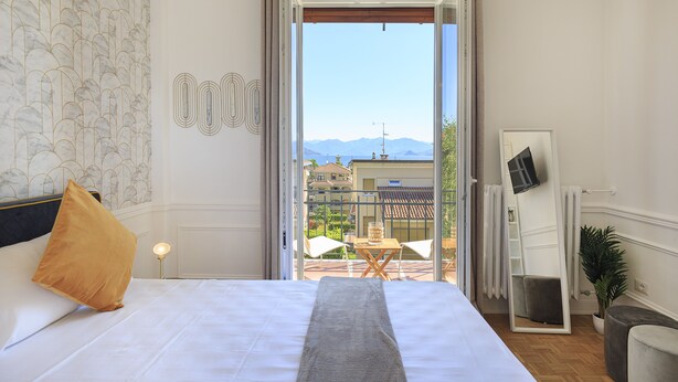 Une chambre avec un grand lit, donnant sur le balcon, et une vue sur la ville en arrière-plan.