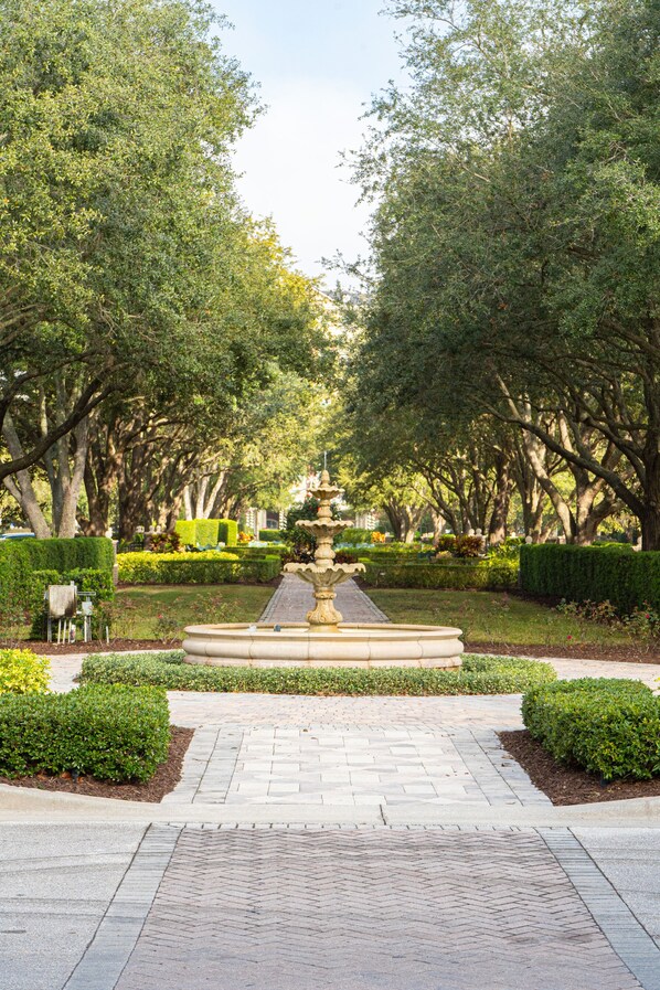 A park pathway leading to a central fountain surrounded by neatly trimmed hedges and trees.