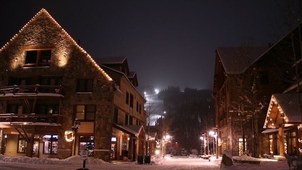 Una strada innevata con edifici dalle facciate in pietra e balconi in legno, illuminata da luci calde.