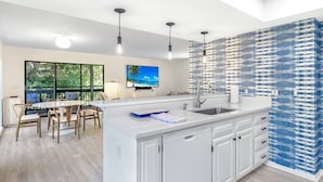 A modern kitchen with a large island, white cabinetry, and a blue and white backsplash. - Sunset Captiva 10 (Captiva)