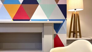 A room with a modern geometric-patterned wall, a white chair, and a floor lamp. - Stylish Studio Apartment in Clifton Village (Bristol)