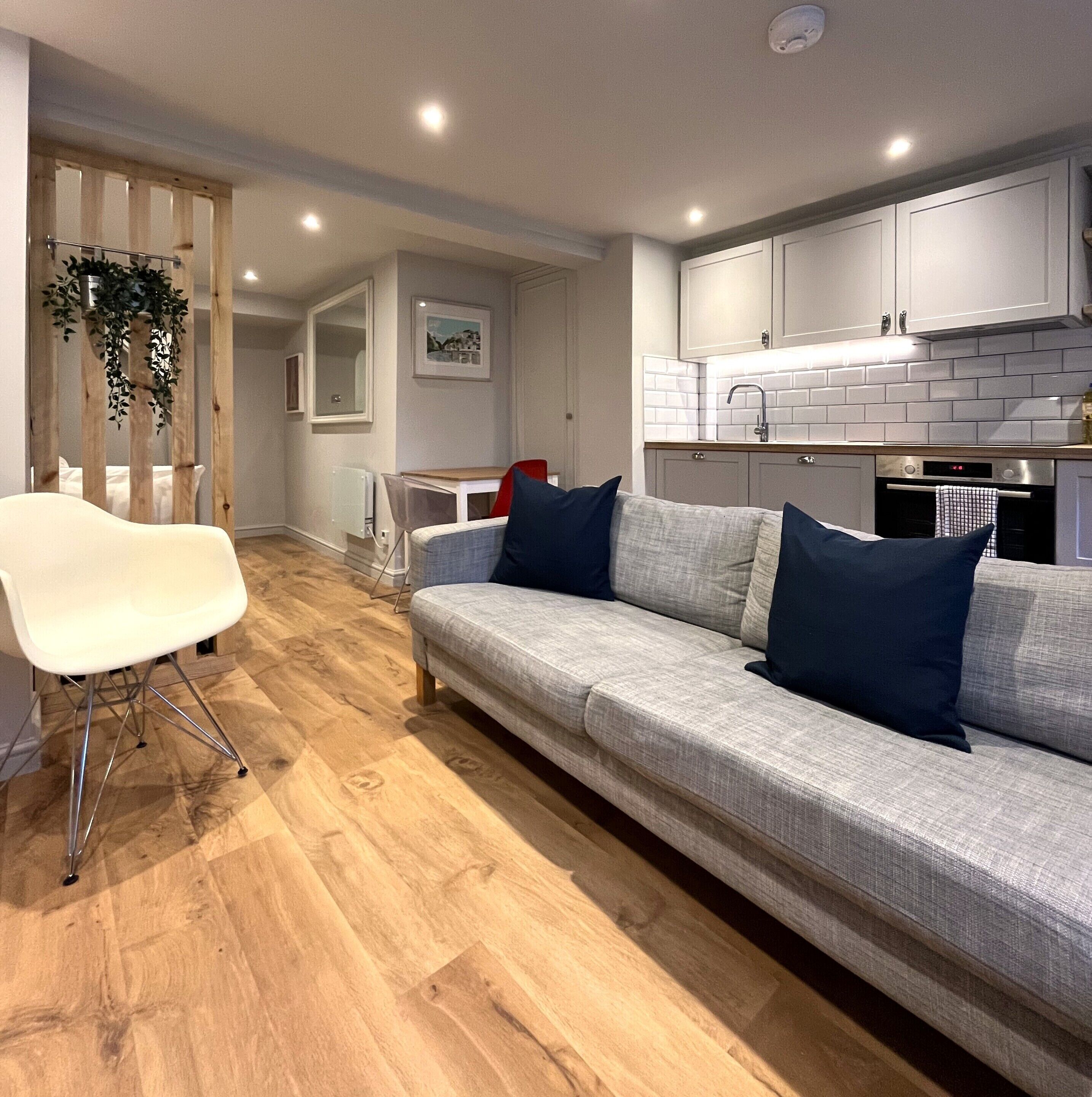 Een moderne woonkamer met een grijze bank, een witte stoel en een houten vloer.