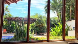 A room with a large window overlooking a garden with palm trees and a pool. - Tamarindo Grand Villa. Oasis at walking distance to Tamarindo Beach! (Tamarindo)