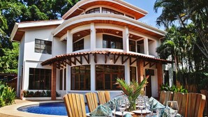 A two-story house with a pool, dining area with chairs and tables, and a covered patio. - Tamarindo Grand Villa. Oasis at walking distance to Tamarindo Beach! (Tamarindo)