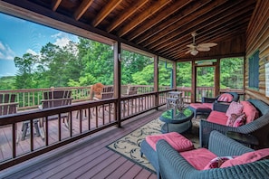 A covered deck with wicker furniture and a view of the forest.